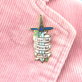 A hard enamel pin on a pink jacket. The pin is in the shape of a dagger and reads Fighting Invisible Battles.