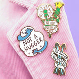 A hard enamel lapel pin being displayed alongside other Jubly-Umph pins. The pin is in the shape of in the shape of two arrows and reads Go Ahead Underestimate Me.