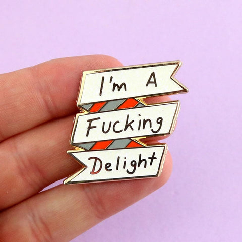 A hard enamel lapel pin being held in a hand. The lapel pin reads I'm A Fucking Delight.