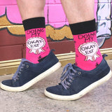 A pair of socks worn with blue shoes. The socks are pink and black and read Doing My Okay-est.