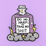 An iron on embroidered patch on purple background. The patch is purple and in the shape of a bottle with clouds and lightning bolts. The pin reads Do No Harm Take No Shit.