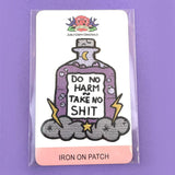 An iron on embroidered patch on Jubly-Umph cardstock. The patch is purple and in the shape of a bottle with clouds and lightning bolts. The pin reads Do No Harm Take No Shit.