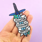 An iron on embroidered patch held in the hand against a purple background. The patch is in the shape of a dagger and reads Fighting Invisible Battles.
