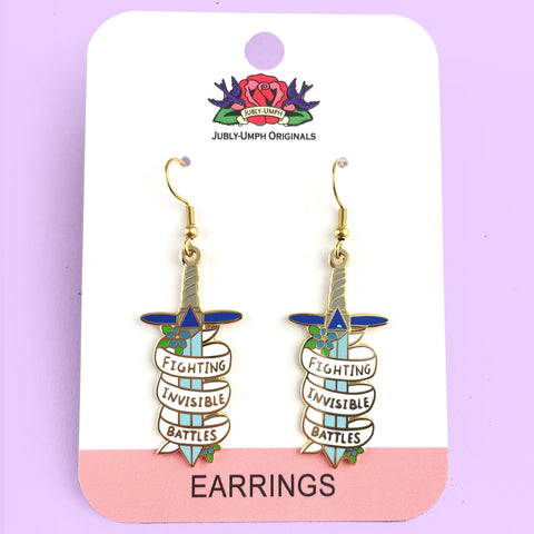 A pair of earrings displayed on Jubly-Umph card stock. The earrings are in the shape of dagger and read Fighting Invisible Battles.