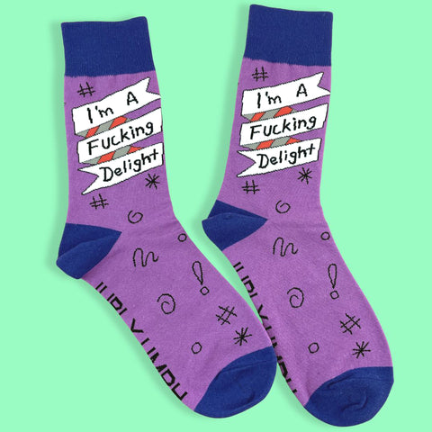 A pair of socks standing against a green background. The socks are purple and blue and read I'm A Fucking Delight.