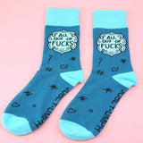 A pair of socks laying flat against a pink background. The socks are blue and light blue and read All Out Of Fucks.